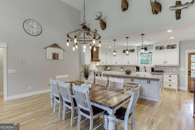 dining space with a high ceiling, light hardwood / wood-style floors, sink, and a chandelier