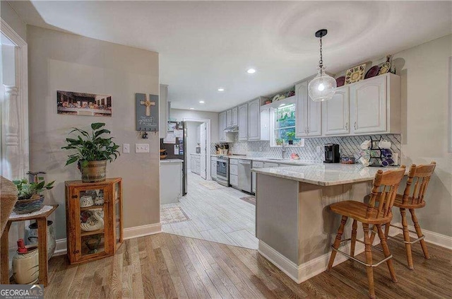 kitchen with hanging light fixtures, dishwasher, sink, tasteful backsplash, and light hardwood / wood-style floors