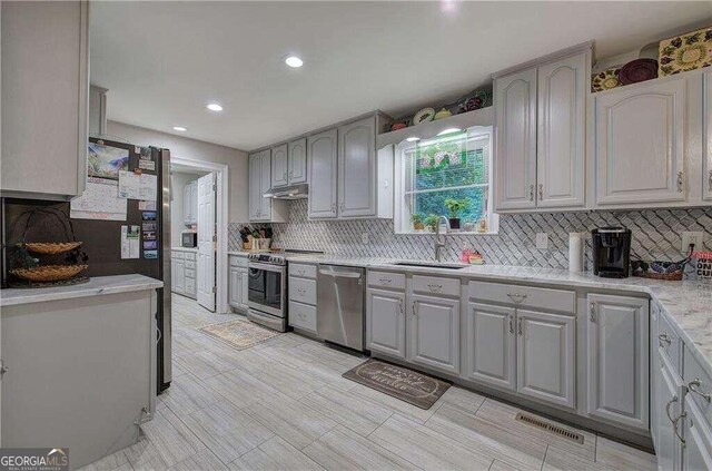 kitchen featuring stainless steel appliances, light tile patterned floors, sink, tasteful backsplash, and gray cabinetry