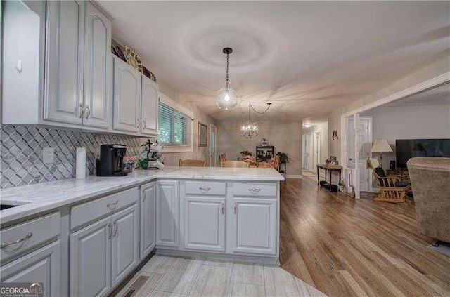 kitchen with light stone counters, decorative light fixtures, light hardwood / wood-style floors, and backsplash