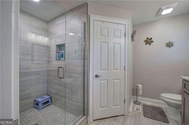 bathroom featuring vanity, toilet, a shower with door, and tile patterned flooring