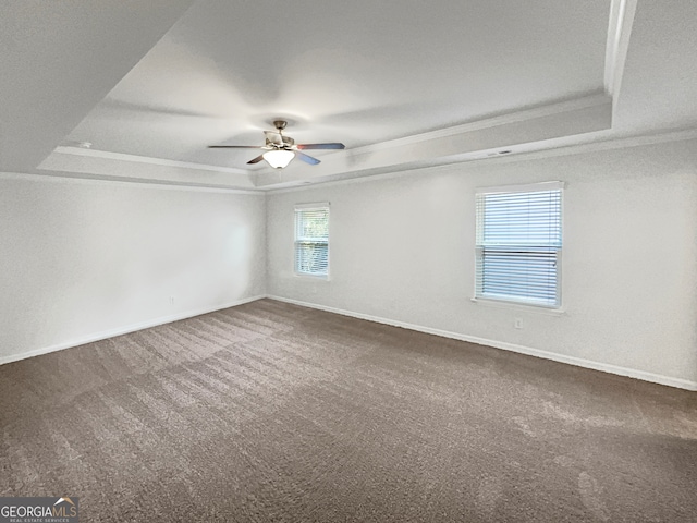 carpeted empty room with ceiling fan, a raised ceiling, and a wealth of natural light