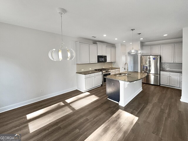 kitchen with stainless steel appliances, decorative light fixtures, sink, a center island with sink, and dark wood-type flooring