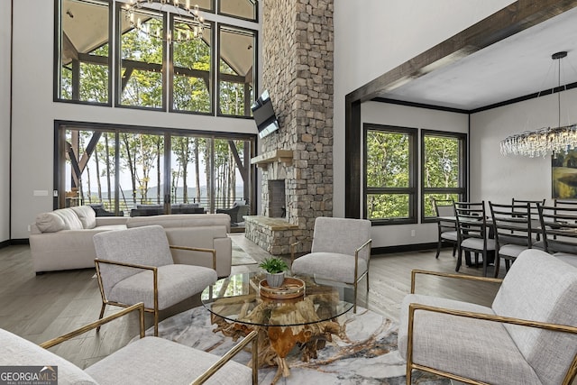 living room featuring a towering ceiling, a stone fireplace, hardwood / wood-style floors, beamed ceiling, and a chandelier