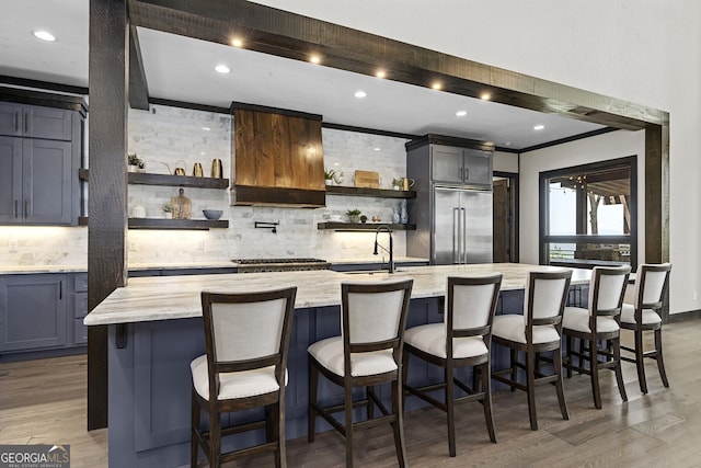 kitchen featuring dark hardwood / wood-style floors, built in fridge, a large island, a breakfast bar, and light stone counters