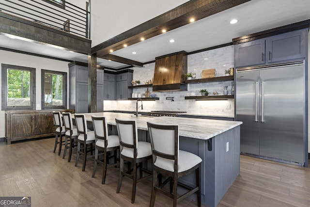 kitchen featuring appliances with stainless steel finishes, an island with sink, light hardwood / wood-style floors, light stone counters, and a breakfast bar