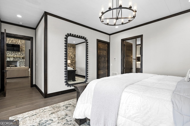 bedroom featuring dark wood-type flooring, crown molding, a chandelier, and a fireplace