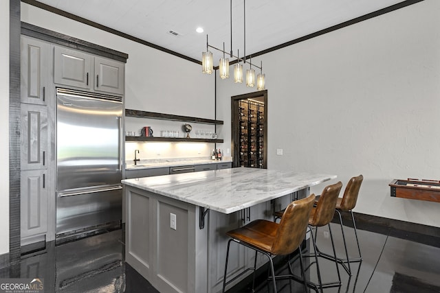 kitchen featuring hanging light fixtures, light stone countertops, ornamental molding, a center island, and built in refrigerator