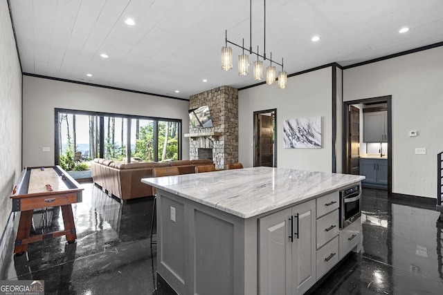 kitchen featuring a fireplace, a center island, light stone counters, white cabinetry, and crown molding