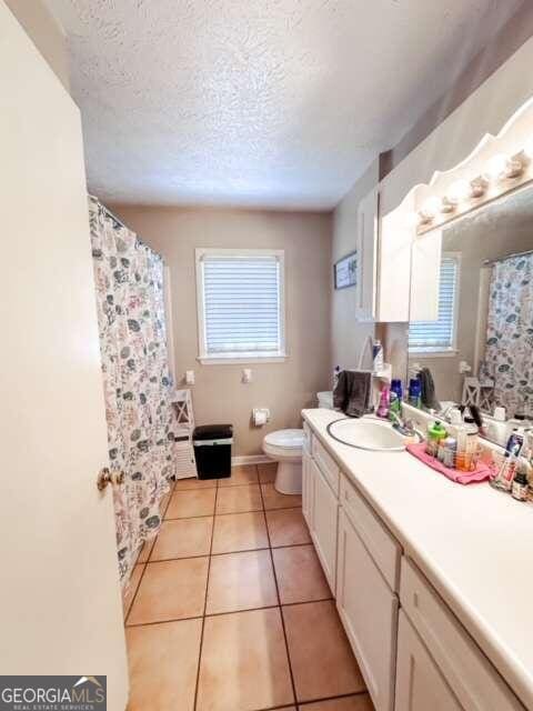 bathroom with tile patterned flooring, vanity, toilet, and a textured ceiling