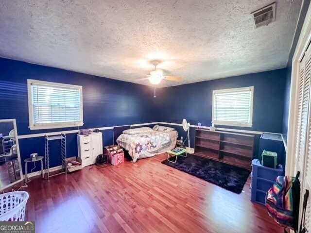 bedroom with hardwood / wood-style flooring, a textured ceiling, ceiling fan, and a closet