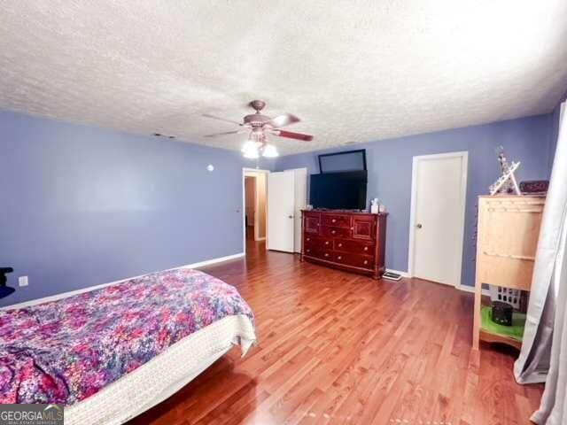 bedroom with a textured ceiling, hardwood / wood-style floors, and ceiling fan