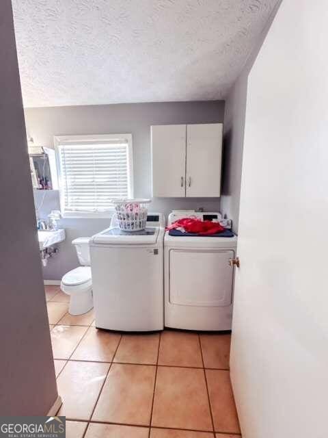 laundry area with separate washer and dryer, a textured ceiling, and light tile patterned flooring