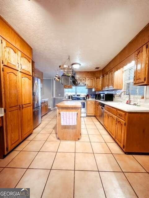 kitchen featuring stainless steel appliances, sink, light tile patterned floors, an inviting chandelier, and a kitchen island