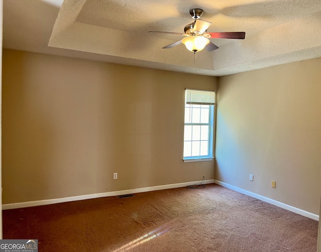 empty room with carpet flooring, ceiling fan, a raised ceiling, and a textured ceiling