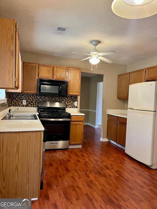 kitchen with stainless steel range with gas cooktop, white fridge, sink, ceiling fan, and dark wood-type flooring