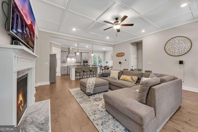 living room featuring ceiling fan, coffered ceiling, a premium fireplace, and hardwood / wood-style floors