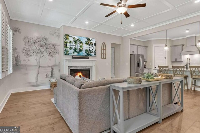 living room featuring coffered ceiling, a premium fireplace, and ceiling fan