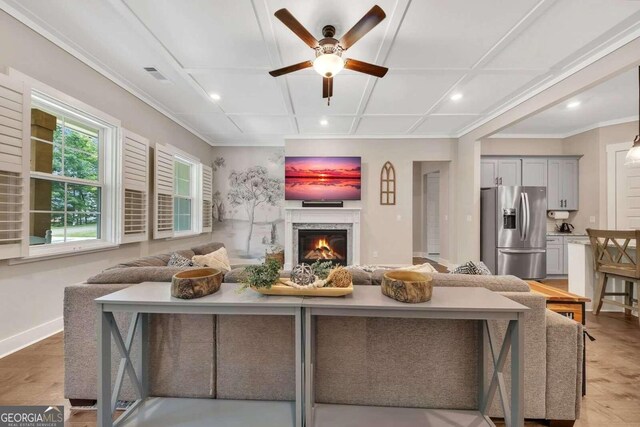 living room with light wood-type flooring, coffered ceiling, a premium fireplace, ornamental molding, and ceiling fan