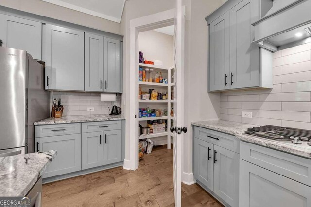 kitchen featuring appliances with stainless steel finishes, light stone countertops, light wood-type flooring, tasteful backsplash, and gray cabinetry