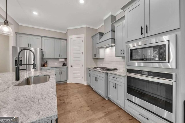 kitchen with stainless steel appliances, custom exhaust hood, light hardwood / wood-style flooring, decorative backsplash, and decorative light fixtures