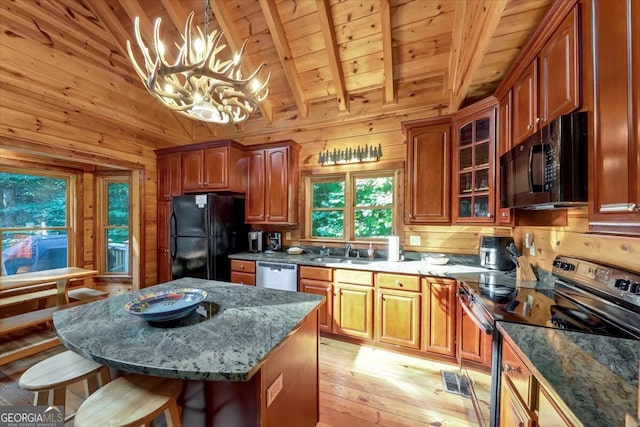 kitchen with black appliances, hanging light fixtures, light wood-type flooring, and wooden walls