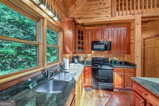 kitchen with wood walls, black appliances, light hardwood / wood-style floors, sink, and dark stone countertops