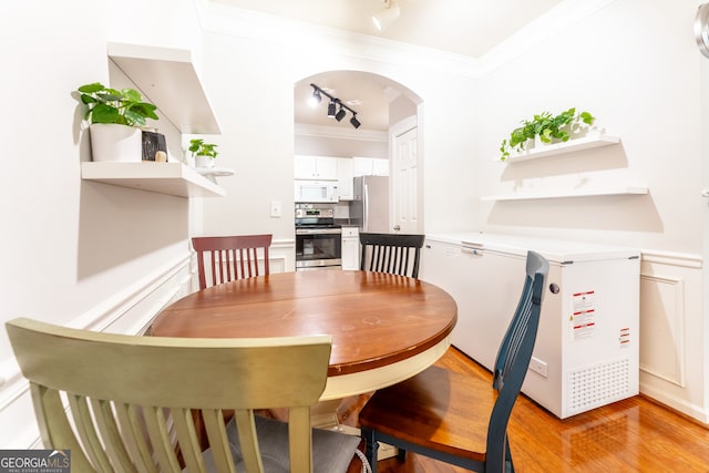 dining room featuring rail lighting, light hardwood / wood-style floors, and ornamental molding