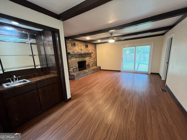 unfurnished living room featuring wood-type flooring, a fireplace, beam ceiling, and ceiling fan