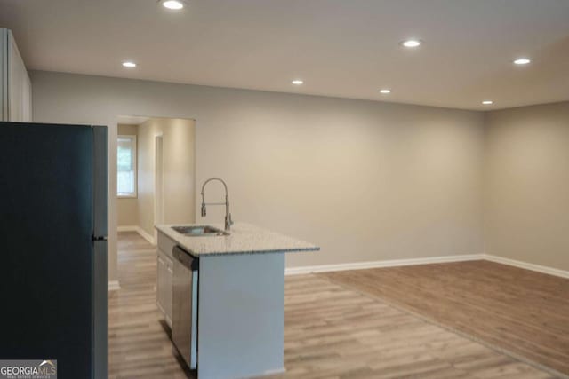 kitchen featuring a kitchen island with sink, dishwasher, sink, light hardwood / wood-style floors, and black refrigerator