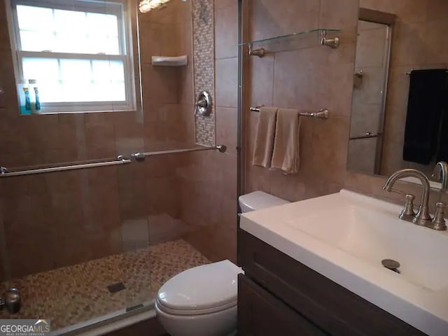 bathroom featuring tile walls, a shower with door, vanity, and toilet