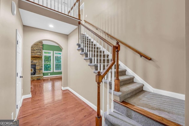 staircase with baseboards, wood finished floors, a high ceiling, a fireplace, and recessed lighting