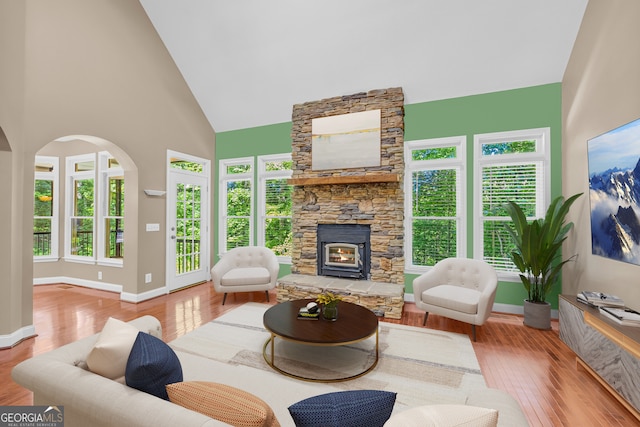 living room featuring a healthy amount of sunlight, light wood-type flooring, high vaulted ceiling, and a wood stove