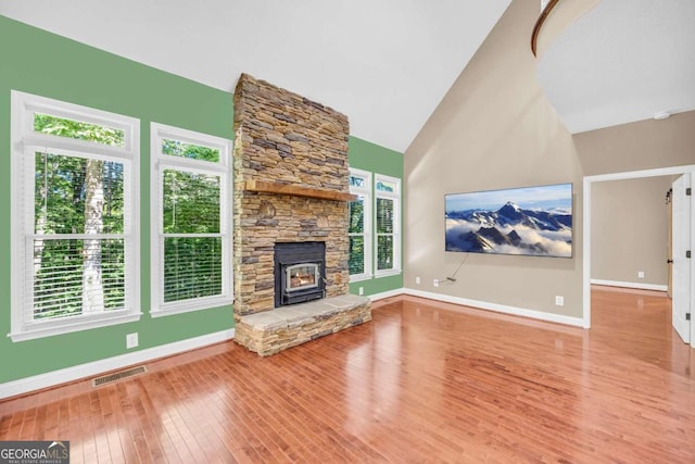 unfurnished living room with visible vents, a stone fireplace, high vaulted ceiling, baseboards, and hardwood / wood-style flooring