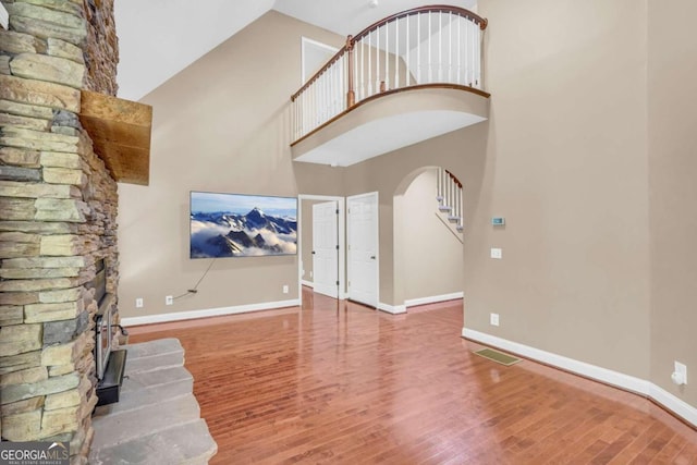 unfurnished living room featuring arched walkways, baseboards, a high ceiling, and wood finished floors