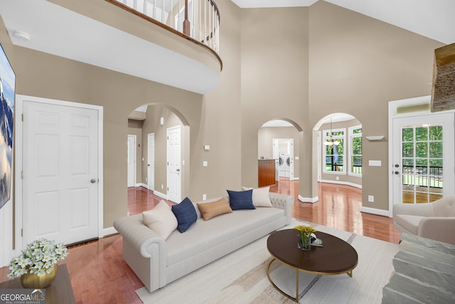 living area with arched walkways, a high ceiling, baseboards, and wood finished floors