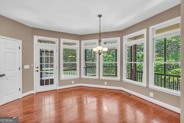 unfurnished dining area featuring an inviting chandelier, visible vents, baseboards, and hardwood / wood-style flooring