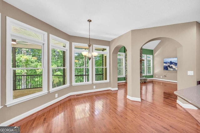 unfurnished dining area with baseboards, arched walkways, visible vents, wood finished floors, and a chandelier