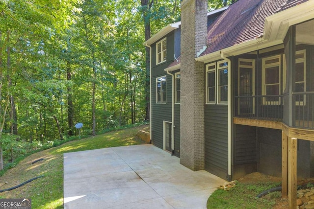 view of property exterior with a sunroom, a shingled roof, a chimney, and a patio