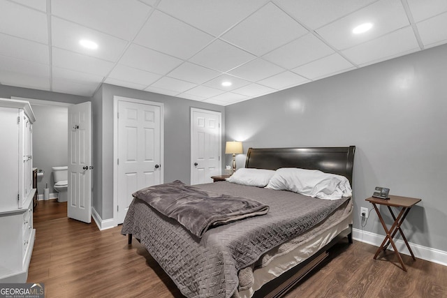 bedroom featuring ensuite bath, dark hardwood / wood-style flooring, and a drop ceiling