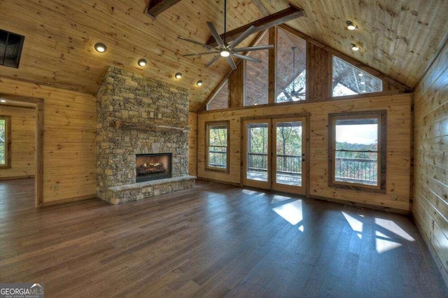 unfurnished living room featuring wood walls, high vaulted ceiling, wood-type flooring, and a stone fireplace