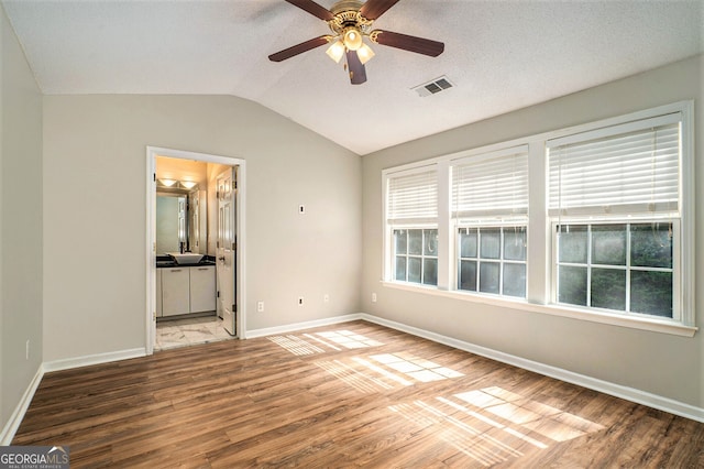 unfurnished bedroom with wood-type flooring, vaulted ceiling, ensuite bathroom, a textured ceiling, and ceiling fan