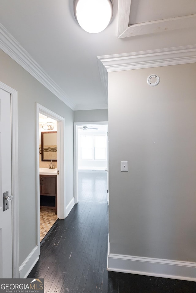 hallway with a sink, ornamental molding, baseboards, and dark wood-style floors