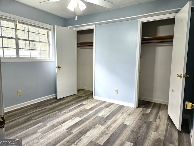 unfurnished bedroom with dark wood-type flooring, ceiling fan, a textured ceiling, and multiple closets