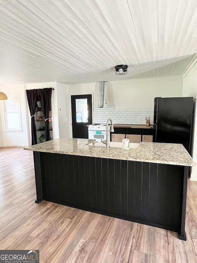 kitchen featuring light stone countertops, light wood-type flooring, a center island with sink, and a healthy amount of sunlight