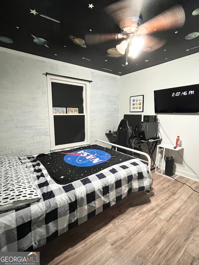 bedroom featuring ceiling fan, hardwood / wood-style flooring, and brick wall