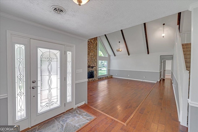 foyer featuring dark hardwood / wood-style flooring, a stone fireplace, lofted ceiling with beams, and a textured ceiling