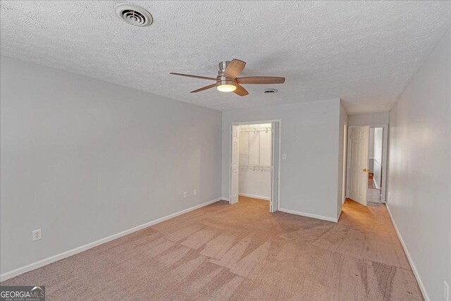 unfurnished bedroom featuring a textured ceiling, a walk in closet, a closet, ceiling fan, and light colored carpet