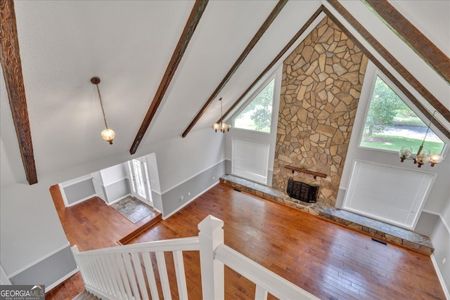 foyer with vaulted ceiling with beams, a stone fireplace, an inviting chandelier, and hardwood / wood-style flooring