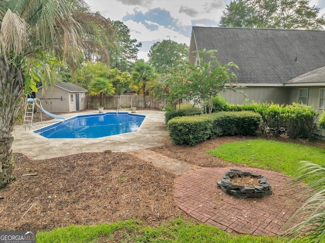 view of swimming pool featuring a patio area, a shed, a diving board, a water slide, and an outdoor fire pit